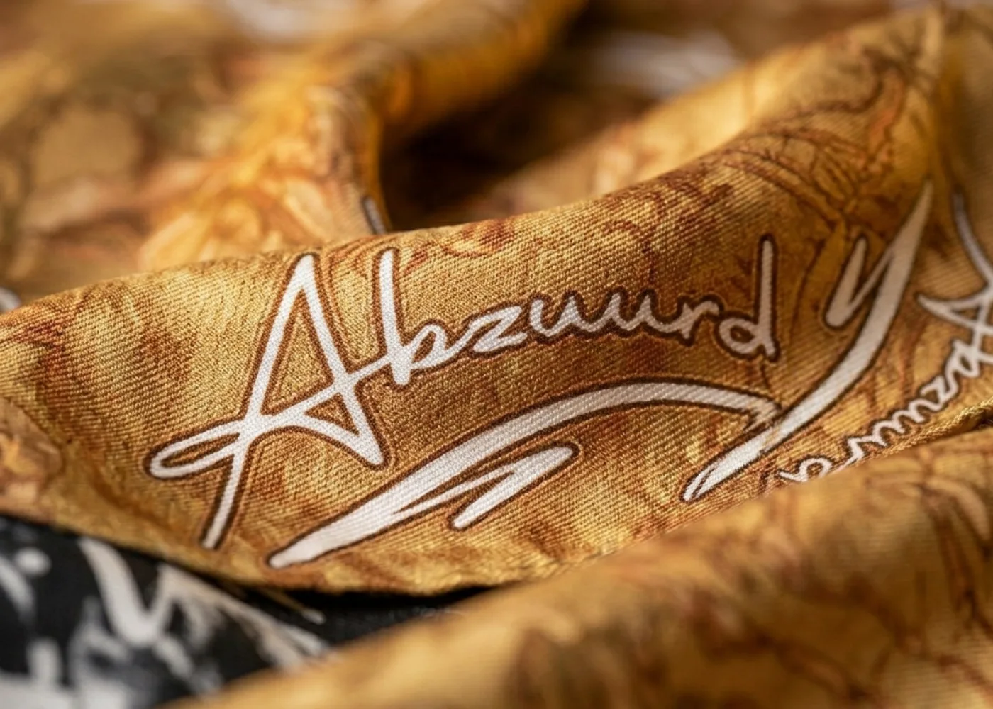 Macro detail of the print: the Abzuurd script in white over baroque scrollwork in gold and tan.